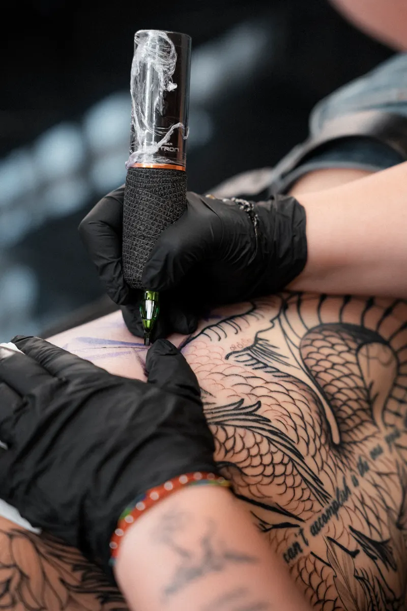 Macro del momento de tatuar: la aguja del cartucho entrando en la piel sobre el stencil, con guantes negros